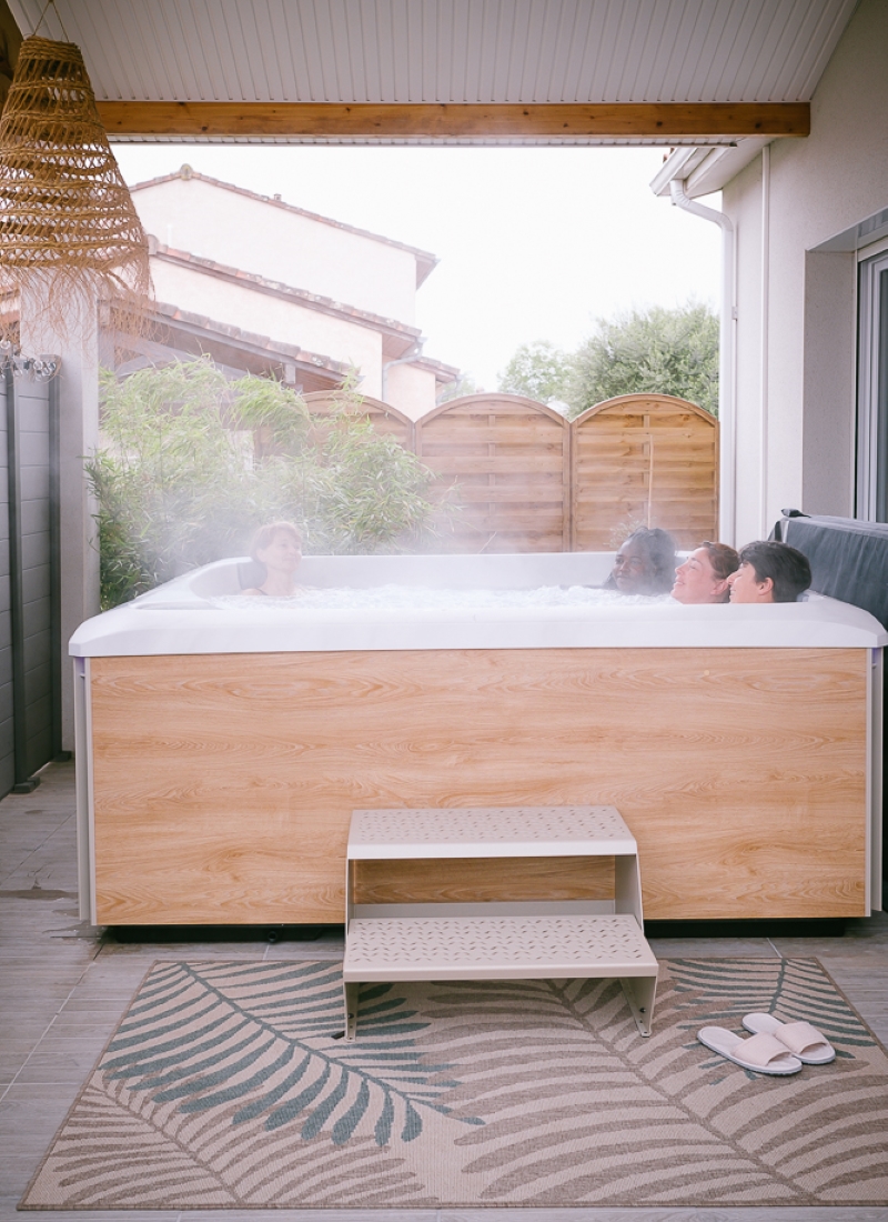 Jacuzzi extérieur chaleureux chez echapetvous à Tarbes, quatre personnes se détendent dans un spa en bois sous auvent